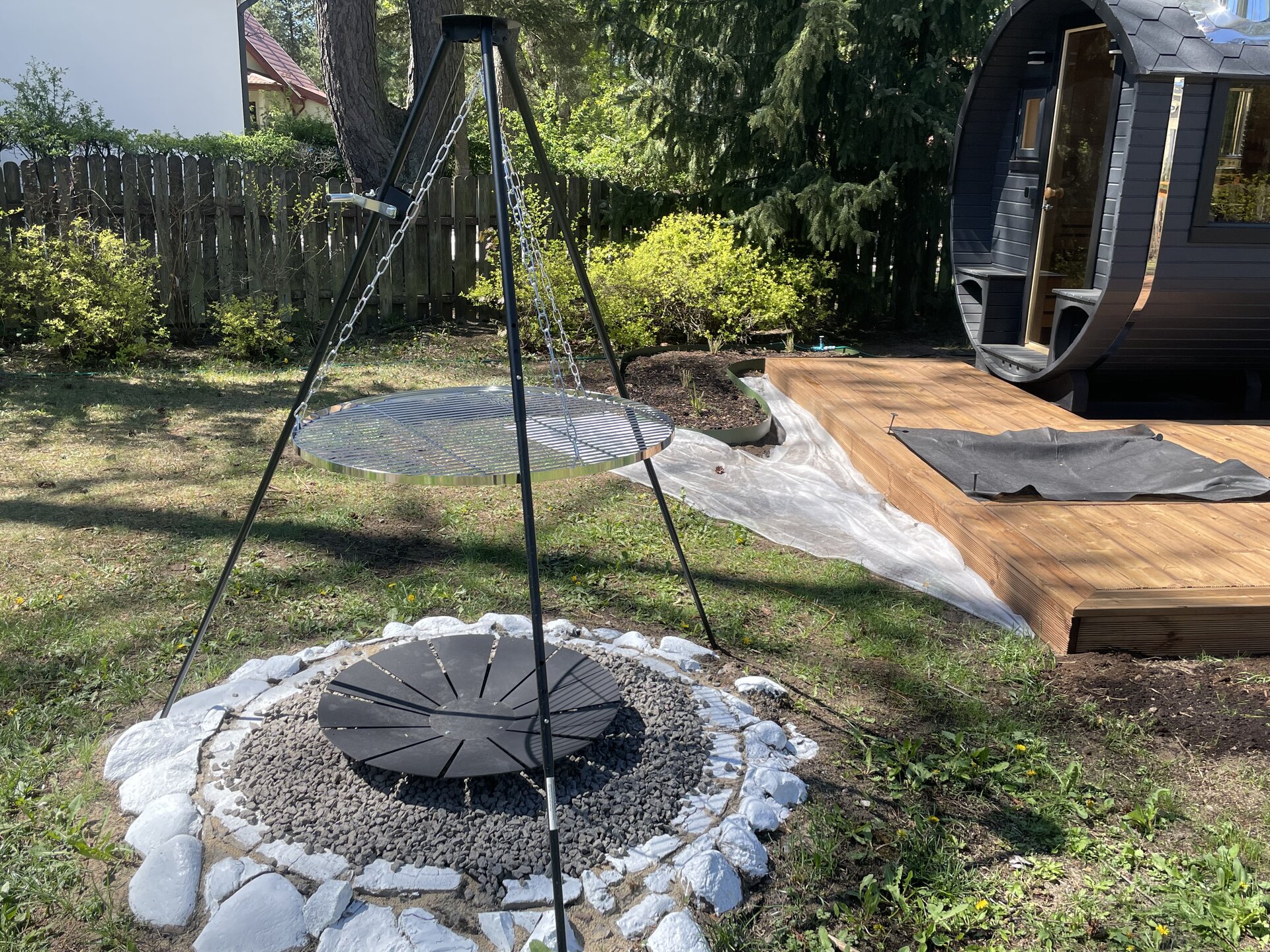 Strefa ogniska z grillem na trójnogu i sauną w tle
